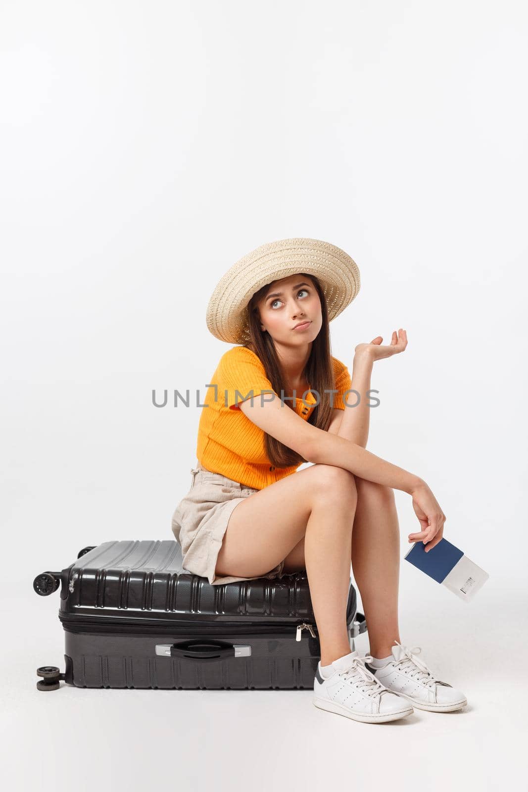 Lifestyle and travel Concept: Young beautiful caucasian woman is sitting on suitecase and waiting for her flight.Isolated over white background.