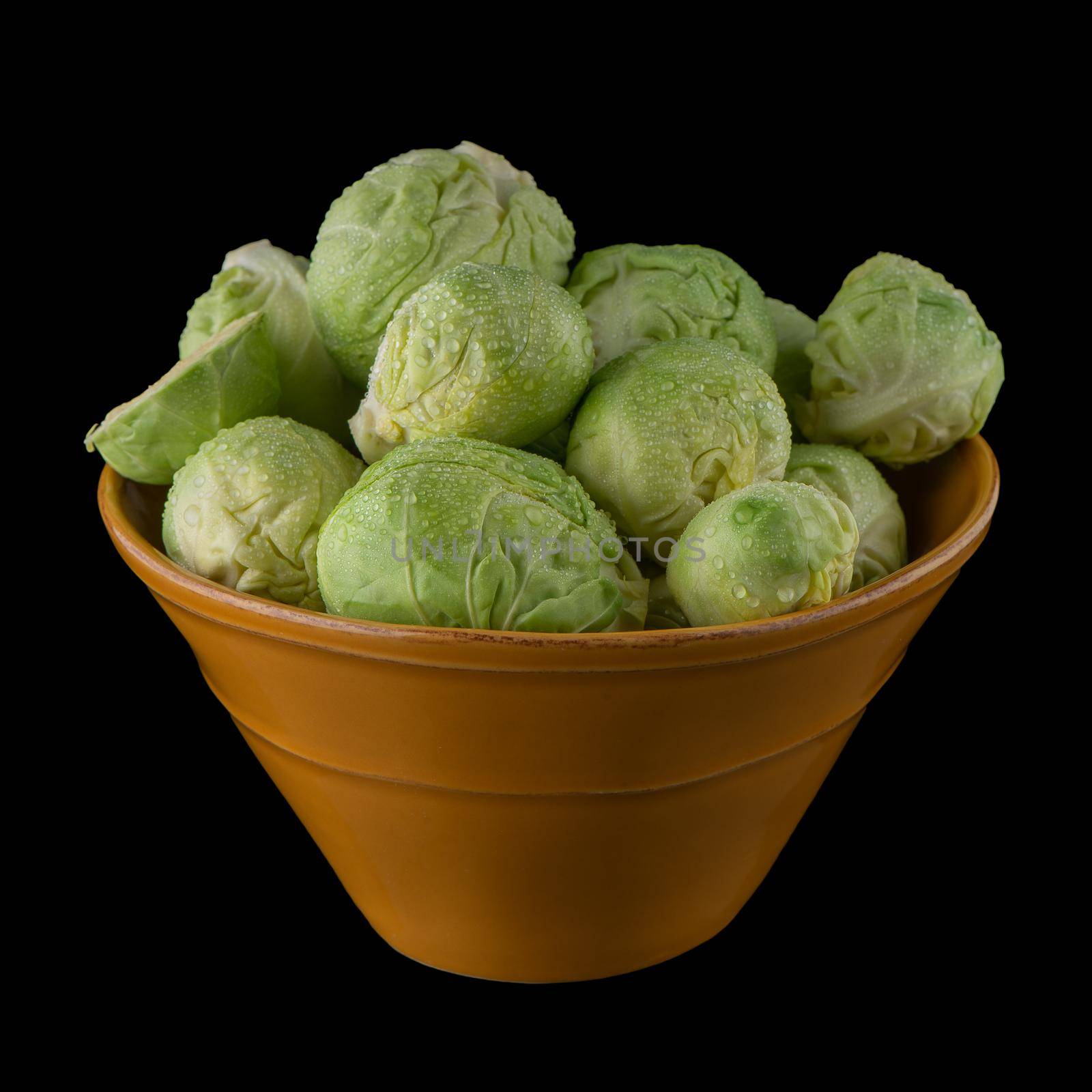 Fresh brussels sprouts on green ceramic bowl isolated on white background.