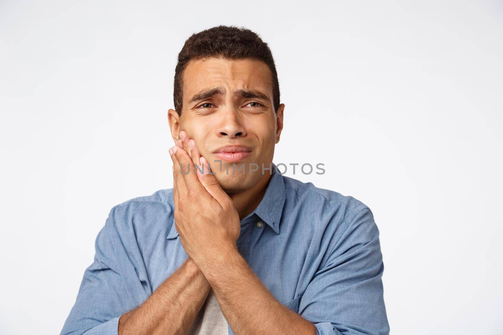 Medicine, people and emotions concept. Upset gloomy young man have discomfort, touch cheek and frowning, need make appointment dentist, suffer toothache, have decay, white background.