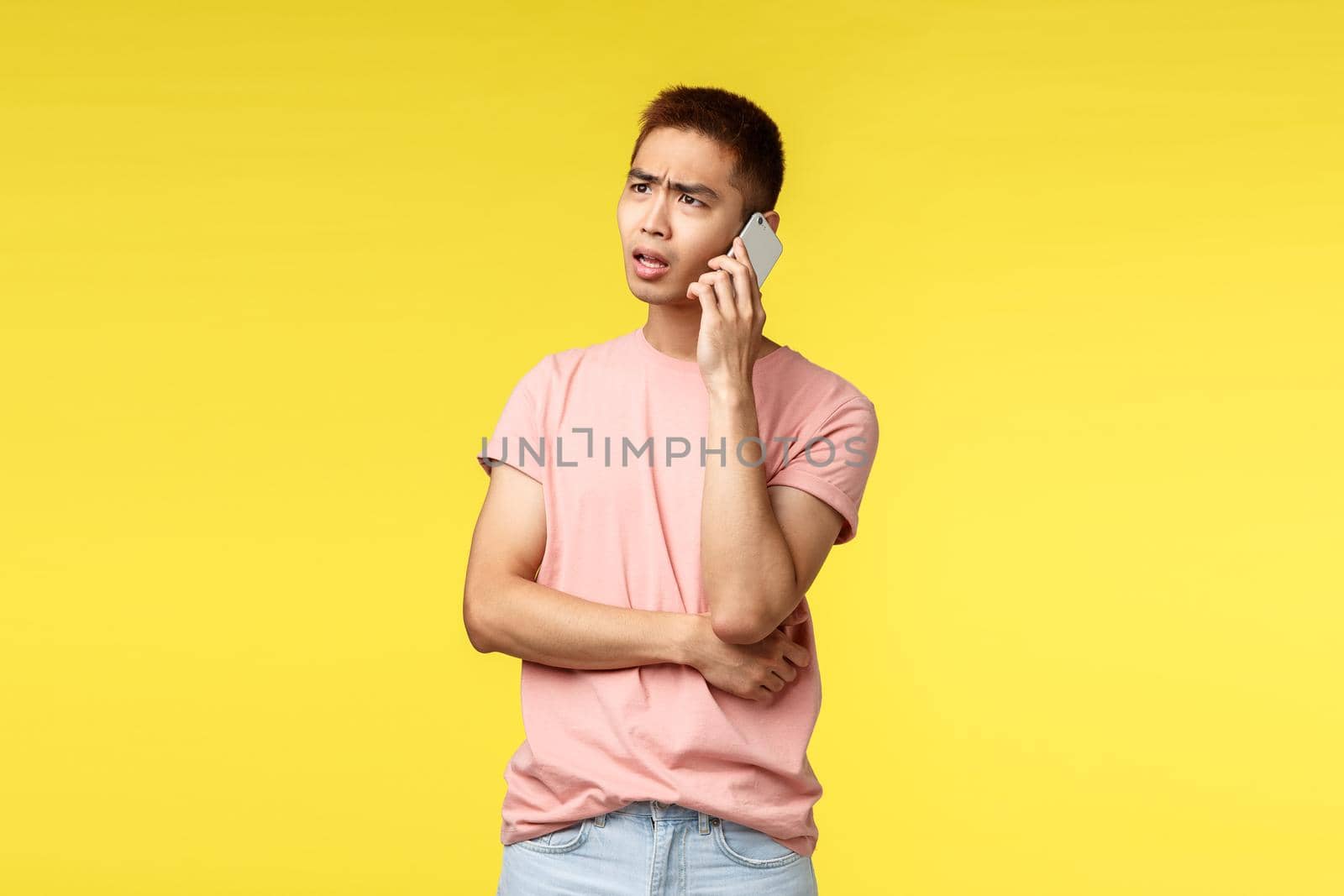 Technology, communication and lifestyle concept. Portrait of frustrated, disappointed asian guy talking on phone, discuss problem on phone, use smartphone and frowning complicated.