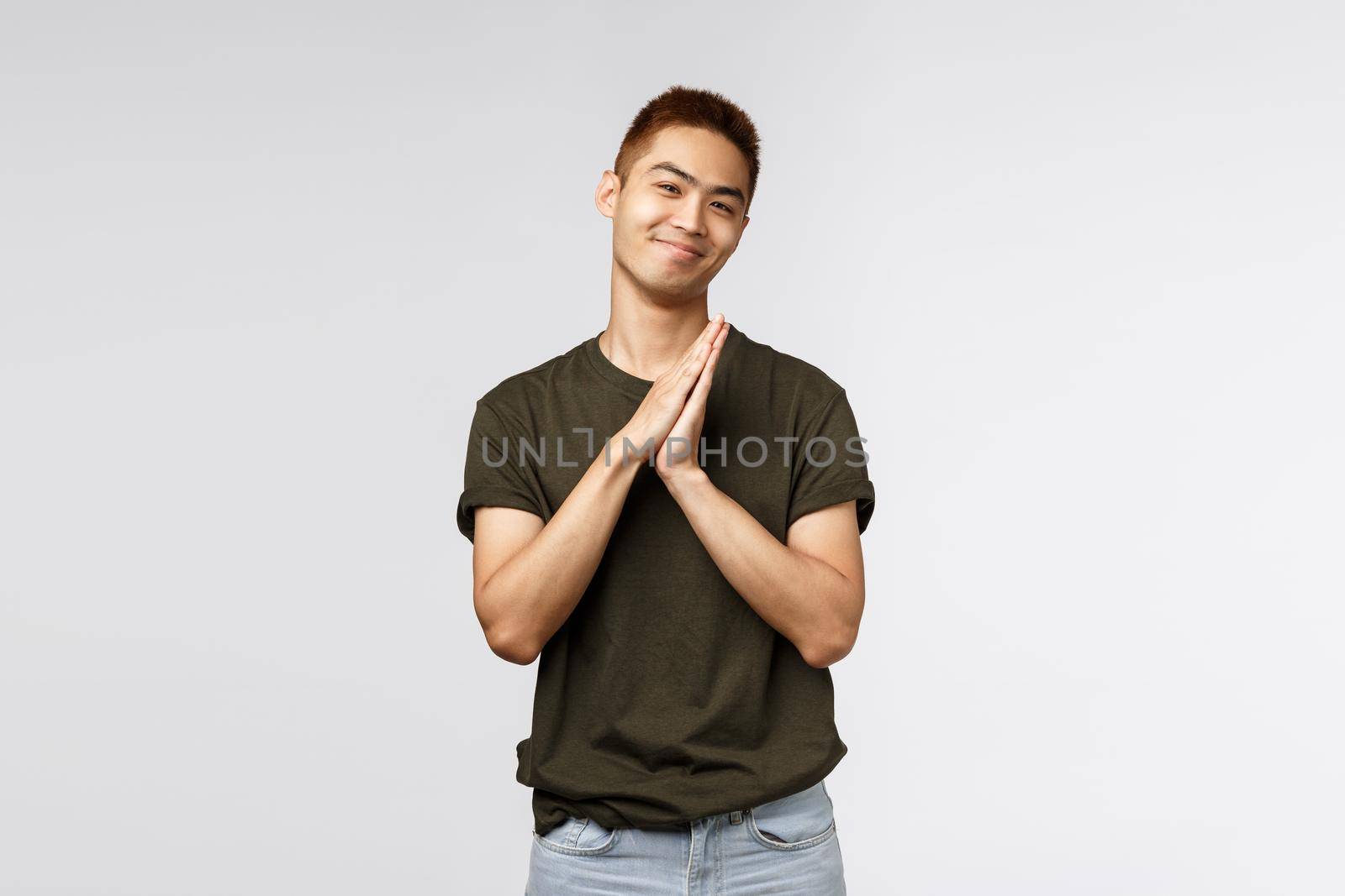 Portrait of cheerful, lovely asian man in greey t-shirt, show namaste gesture, asking for favour or appreciate help, clasp hands together and smiling, praying over grey background.