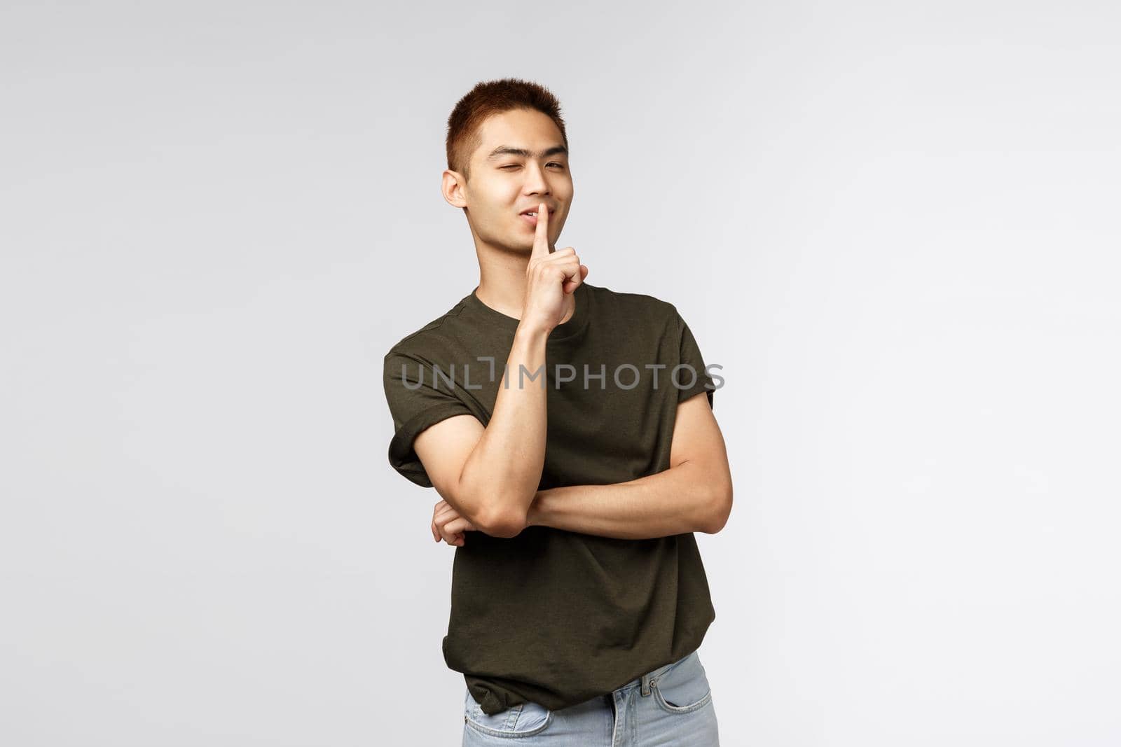Portrait of cheeky handsome asian boyfriend prepared surprised, wink sassy and assured, smiling as shushing, promise keep secret, ask be quiet and not talk about it, grey background.