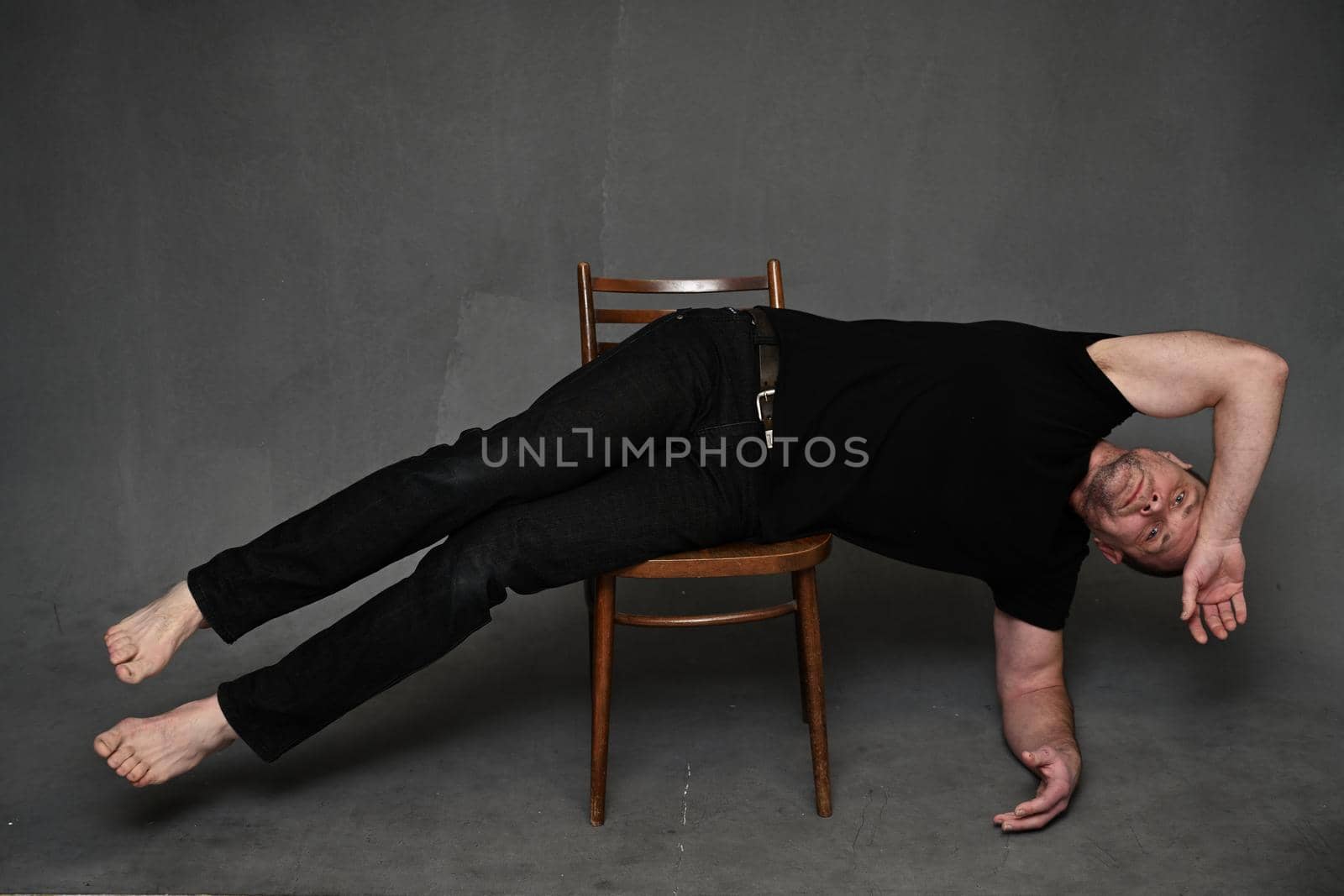 Middle-aged caucasian man on a gray background looking directly at the camera while lying on a chair