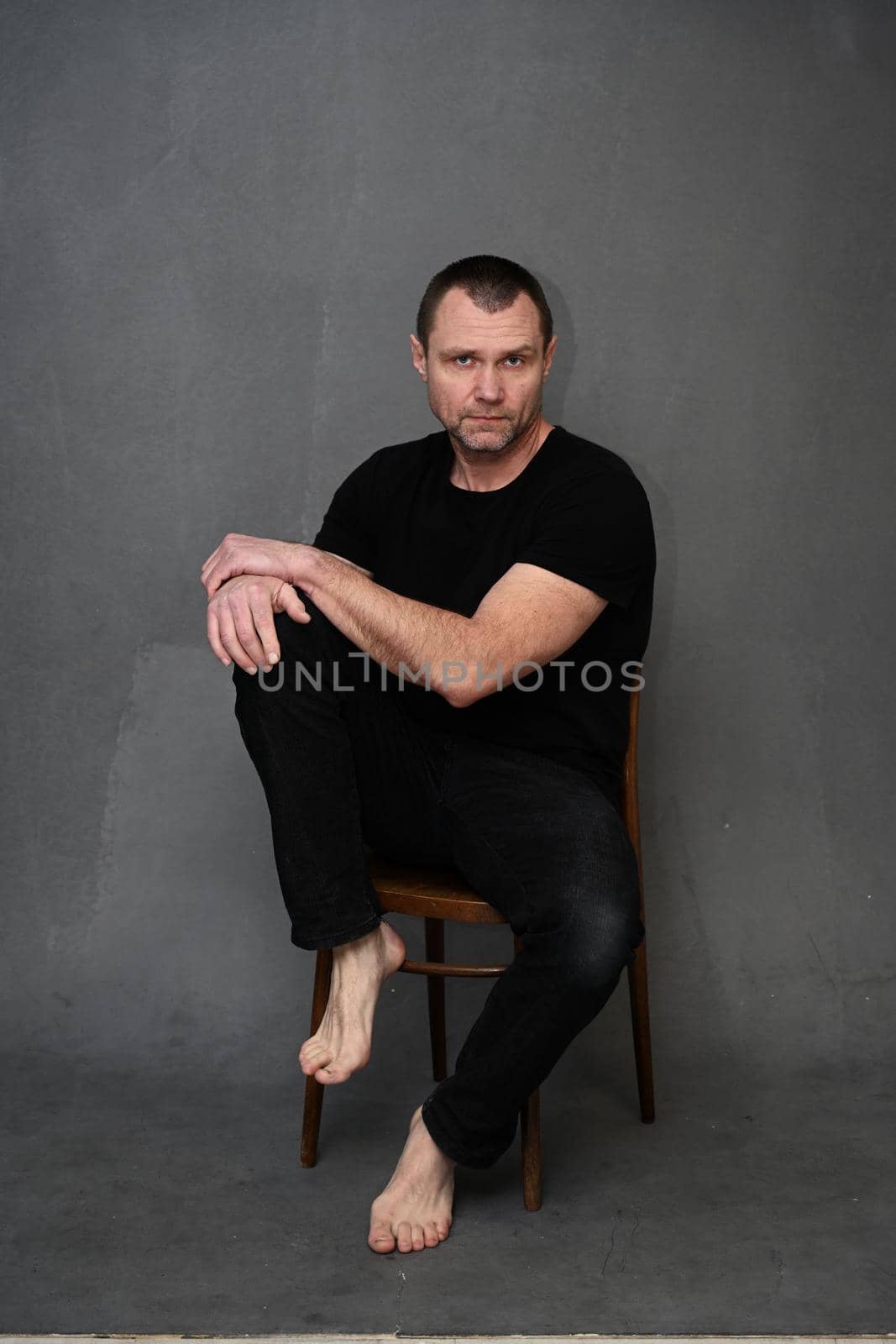 Serious adult male man on gray background looking directly at camera while sitting on chair