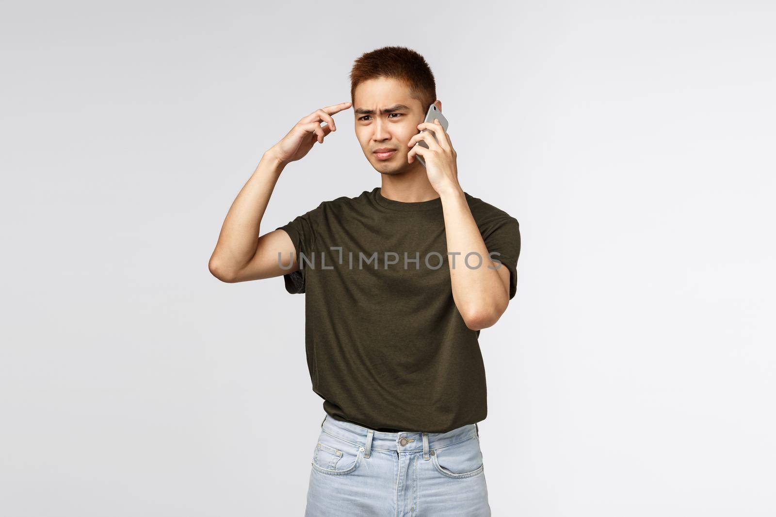 Technology, online lifestyle and communication concept. Portrait of frustrated and confused, judgemental asian guy think speaker is stupid or crazy, talking on phone and cringe displeased by Benzoix