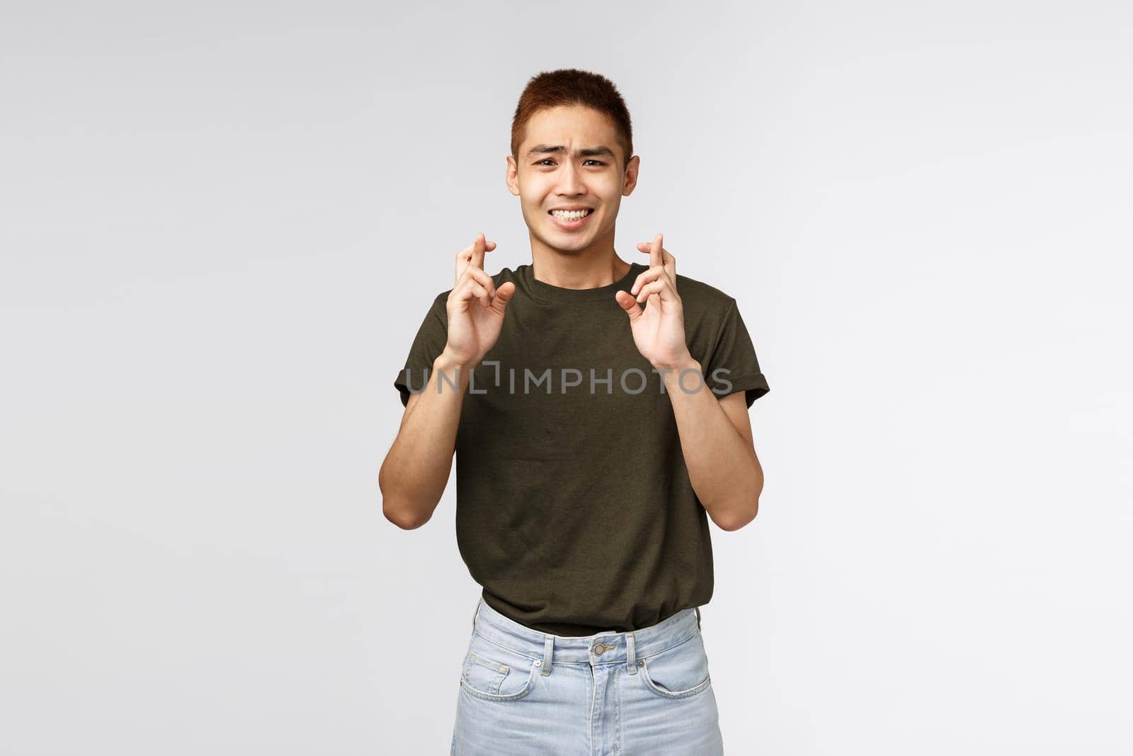 Male student having high hopes about entering university or passing exam. Portrait of happy anticipating man cross fingers for good luck, clenching teeth and look tensed camera by Benzoix