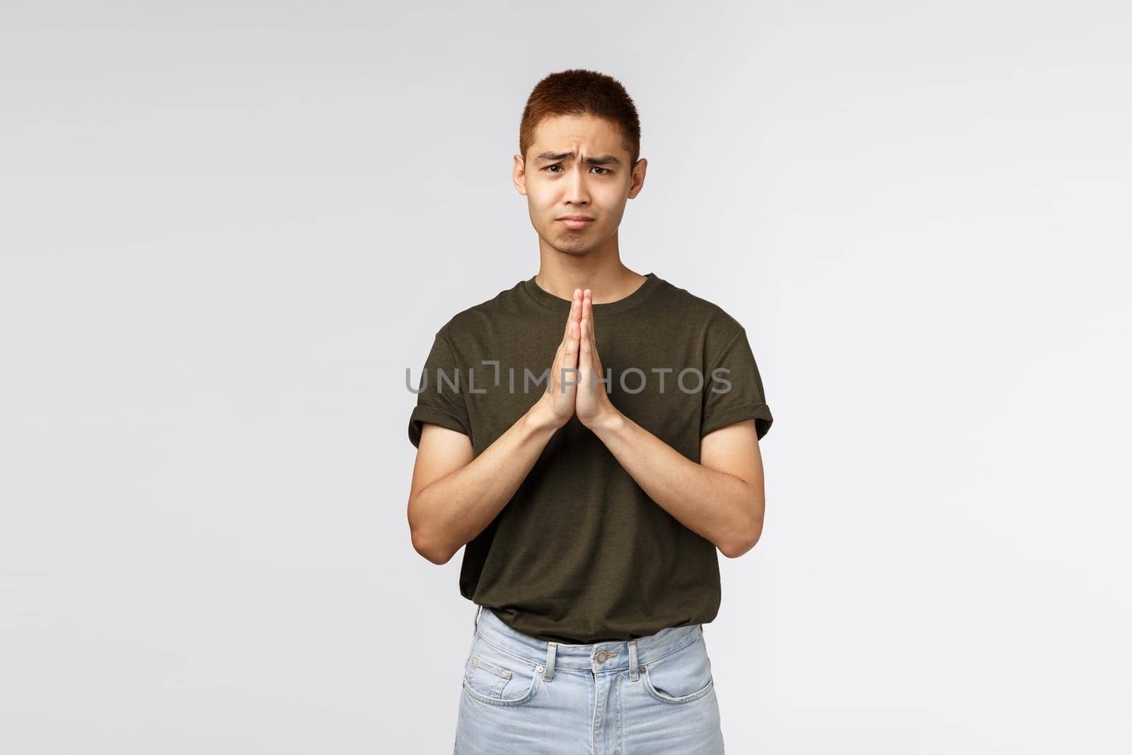 Please help me out. Portrait of hopeful clingy cute asian man asking apology, clasp hands together in pray, gloomy looking camera pleading, begging you, standing grey background.