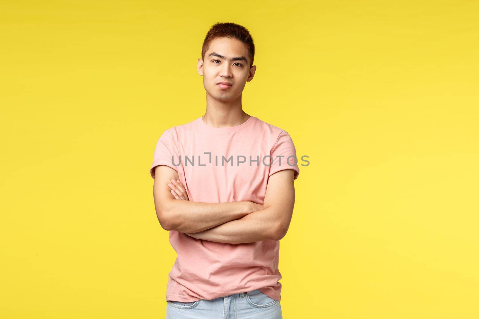 Guy dont buy someone telling lie. Portrait of skeptical, annoyed asian hipster guy in pink t-shirt, cross arms chest, look judgemental with disbelief, standing yellow background disappointed.