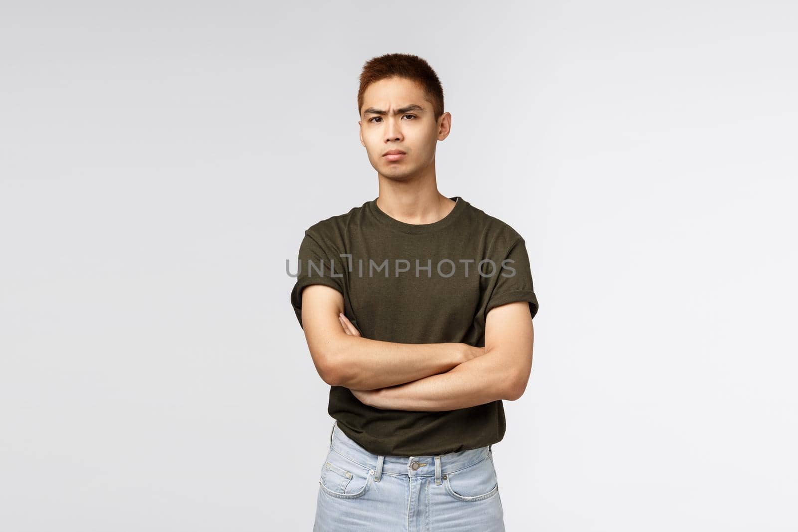 Suspicious serious-looking asian man, cross arms chest and frowning, stare camera with disbelief, dont buy any word person saying, standing tensed and disappointed over grey background.