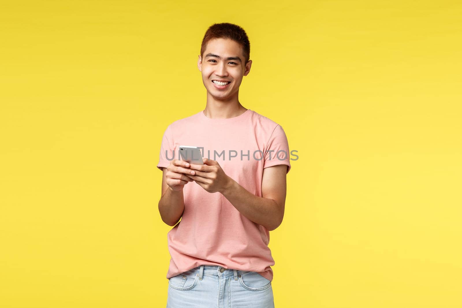 Technology, communication and lifestyle concept. Portrait of cheerful, enthusiastic hipster guy, asian male in pink t-shirt using mobile phone, laughing at camera, staying online, order delivery by Benzoix