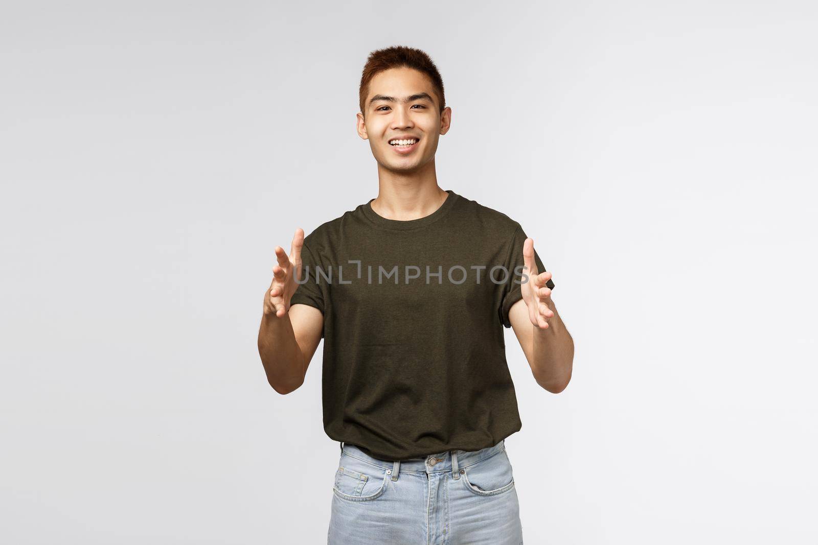 Portrait of cheerful happy healthy asian man, young guy receiving parcel from online delivery while sitting at home quarantine covid19, reaching hands to take products, grey background.