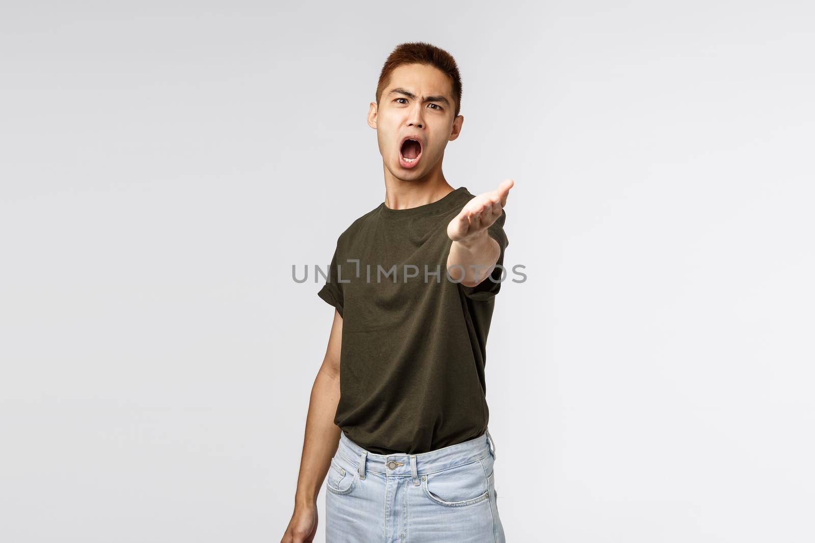 Portrait of angry complaining asian man pointing hand at camera with aggressive distressed look, disappointed arguing, received wrong parcel, being outraged standing grey background.