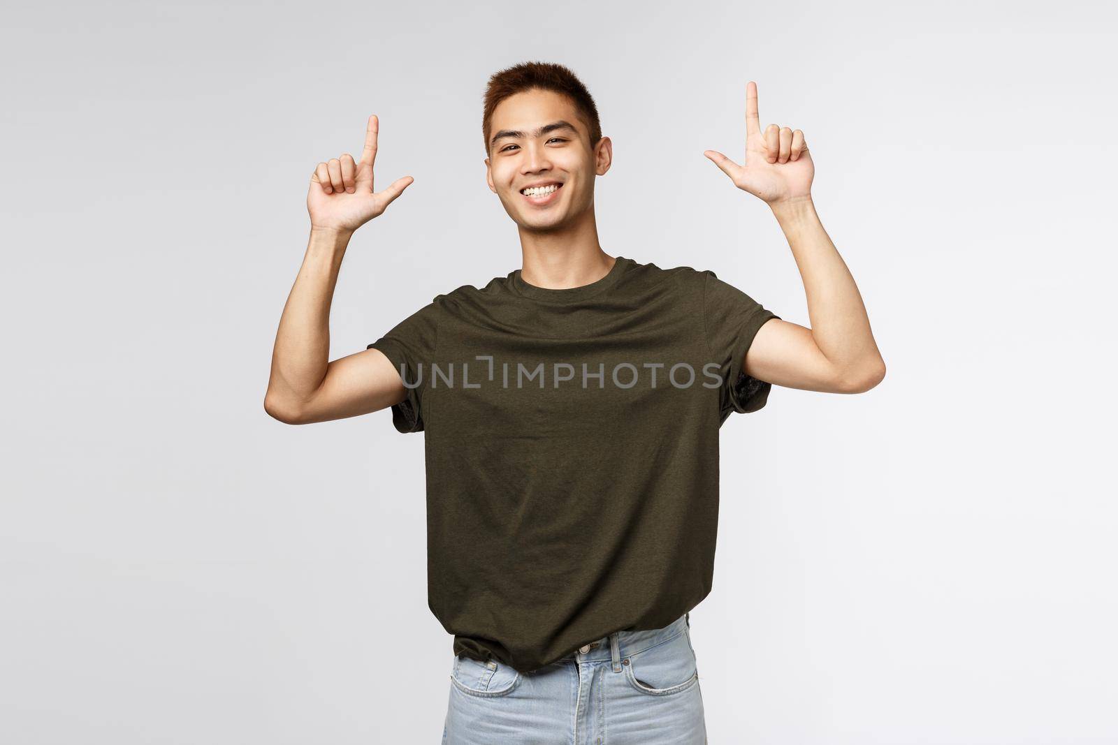 Portrait of proud happy, smiling asian young man, teen guy pointing fingers up and grinning at camera satisfied, person showing way to promo, advertise product or company banner.