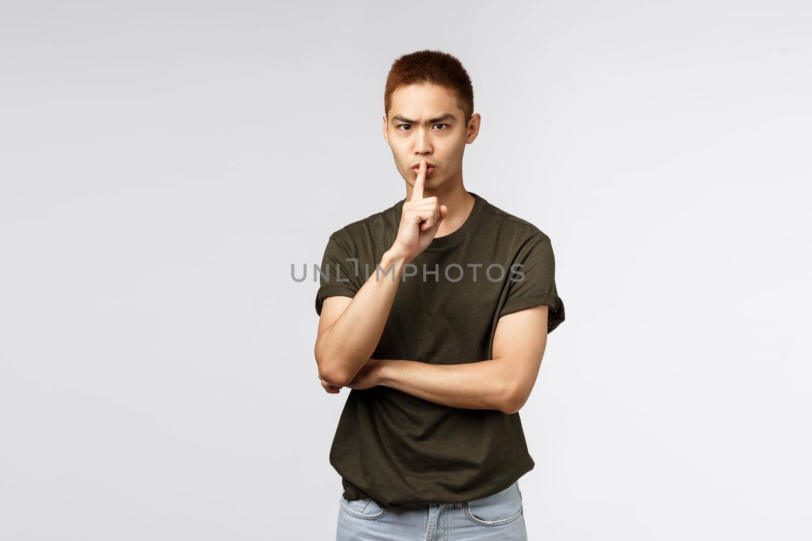 Portrait of angry serious-looking, aggressive asian young guy shushing with annoyed face, press finger to lips, clench teeth and grimacing displeased, scolding person being too loud and noisy.