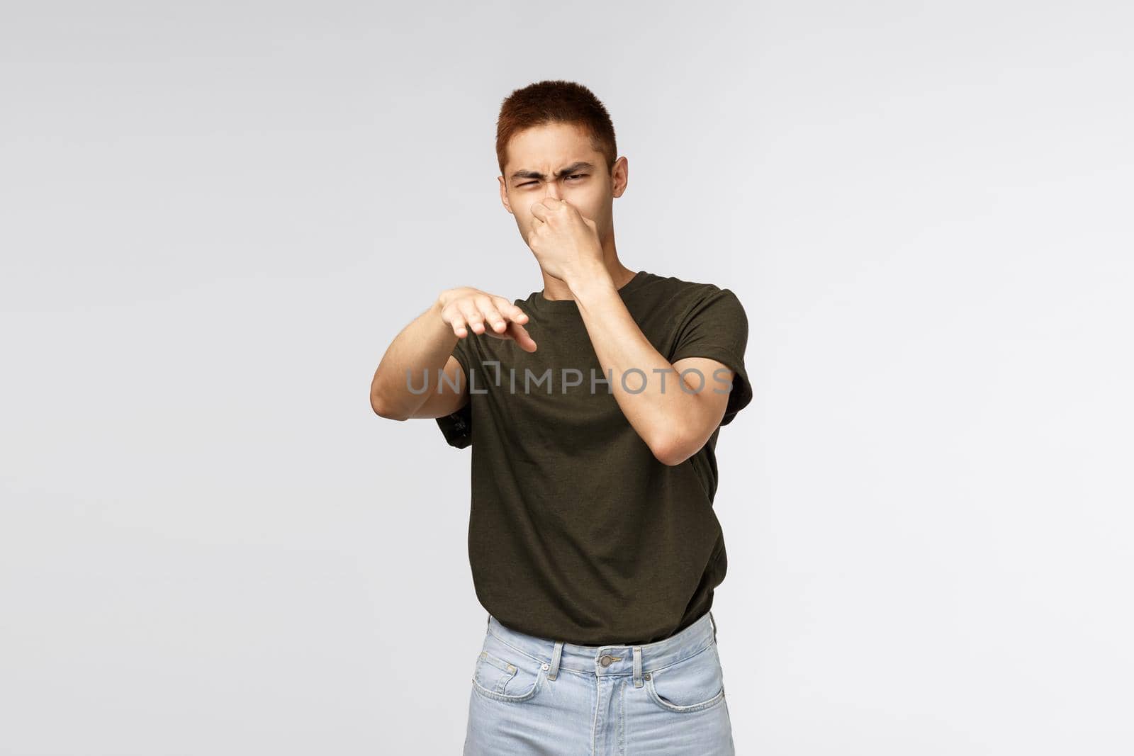 Guy its gross, stinks. Portrait of displeased and disgusted young asian man shut nose and waving with disappointment and aversion at person who smells awful, standing grey background by Benzoix
