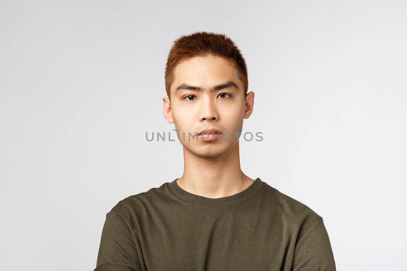 Close-up portrait of serious-looking japanese guy in green t-shirt, look serious and determined, listen to tutor during online lecture while social-distancing at home, standing grey background.