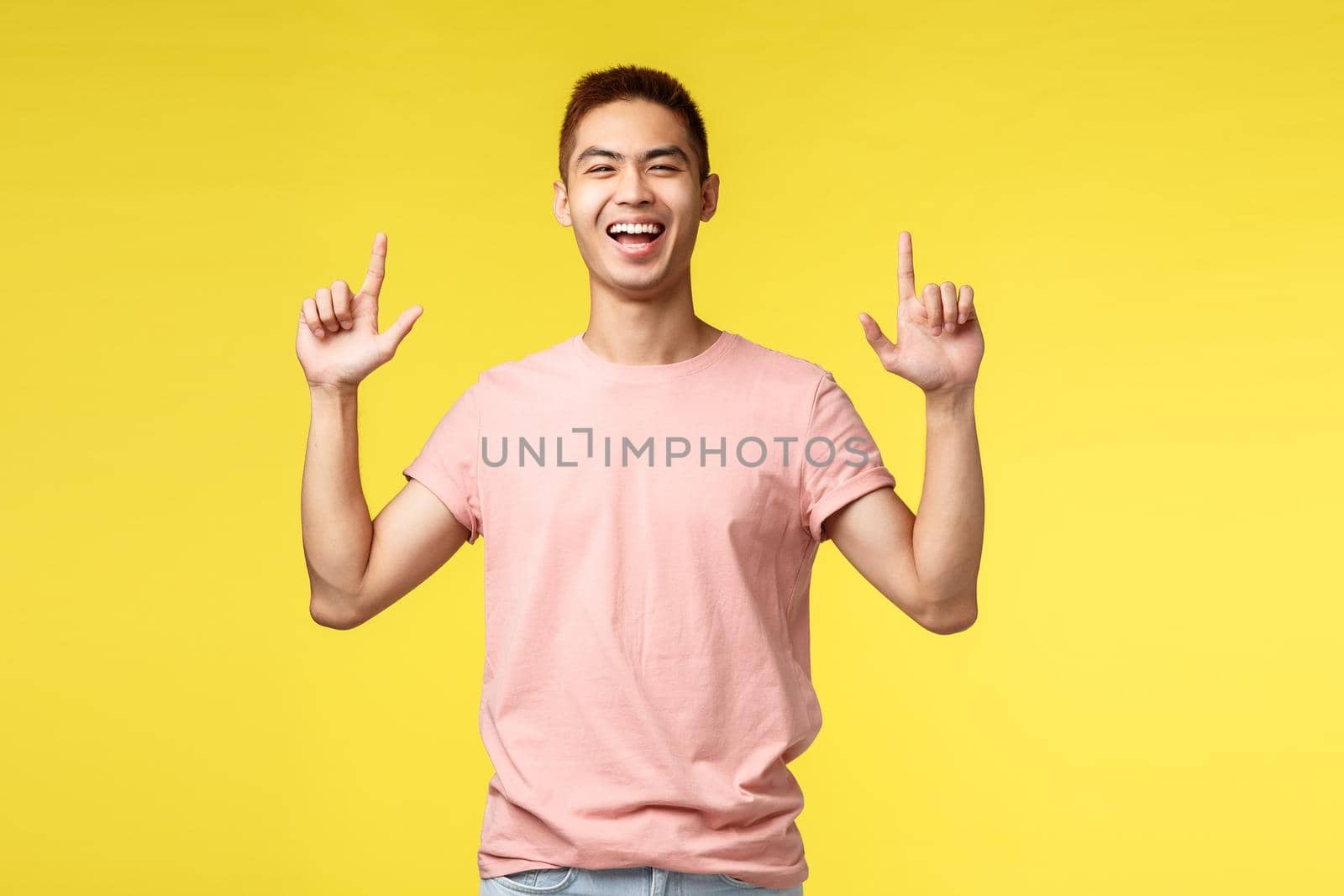 People, different emotions and lifestyle concept. Portrait of joyful handsome young man, asian guy smiling broadly, pointing fingers up and laughing as showing way to product, invite visit event.