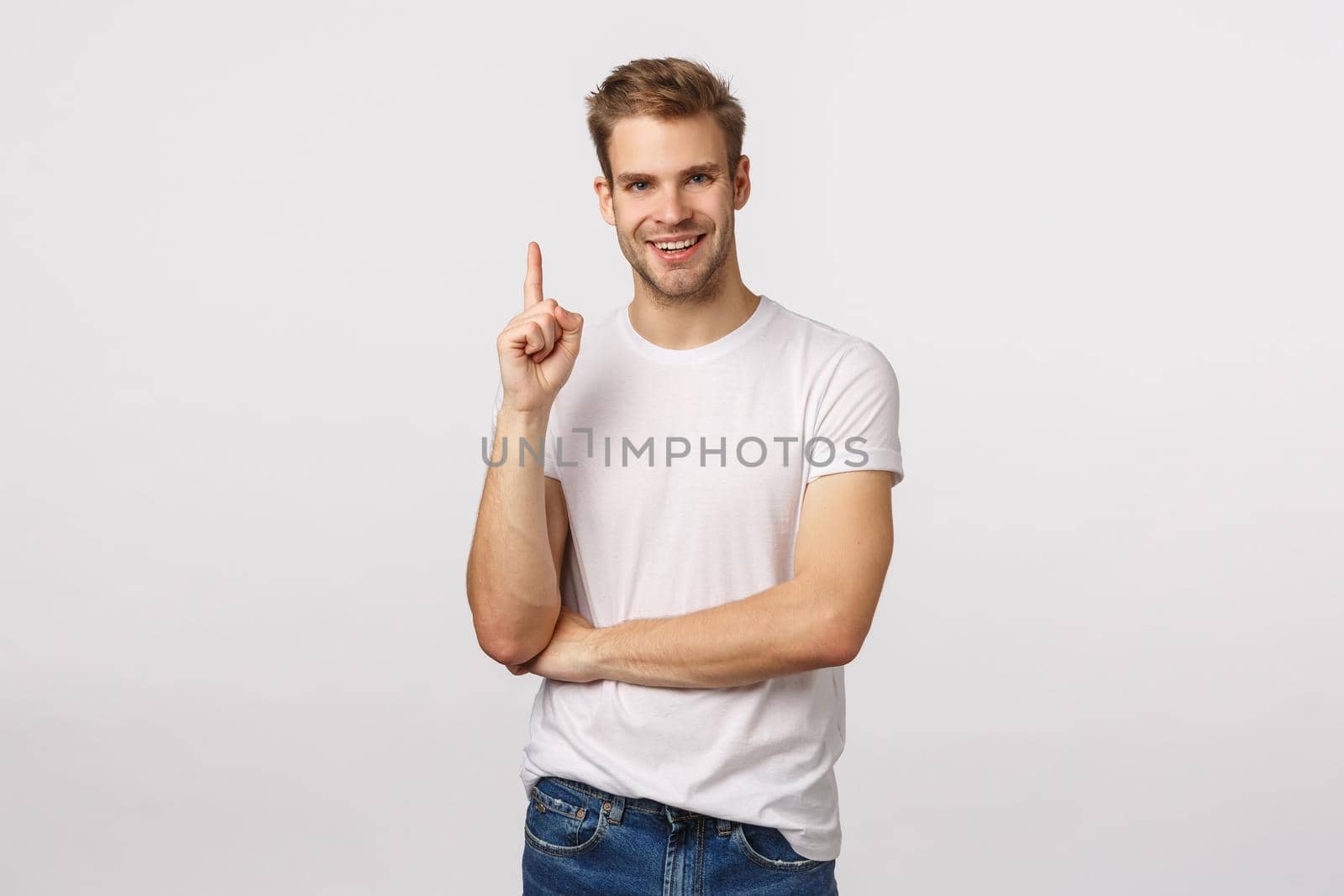 Guy made up excellent idea. Attractive smiling blond man in white t-shirt, bristle, raise index finger, pointing up or have suggestion, express own opinion, make eureka gesture, white background.