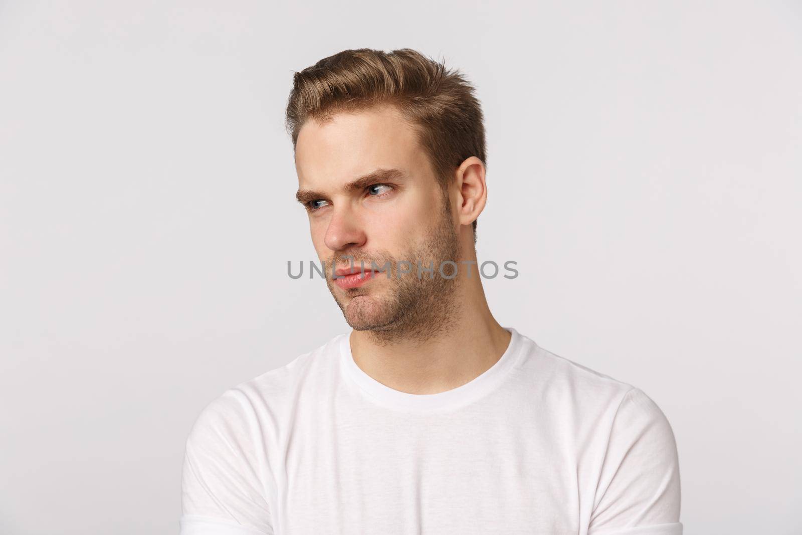 Angry and displeased caucasian bearded blond young man feeling jealous or aggressive towards coworker, look left with contempt or disdain, frowning, pouting offended, standing white background.