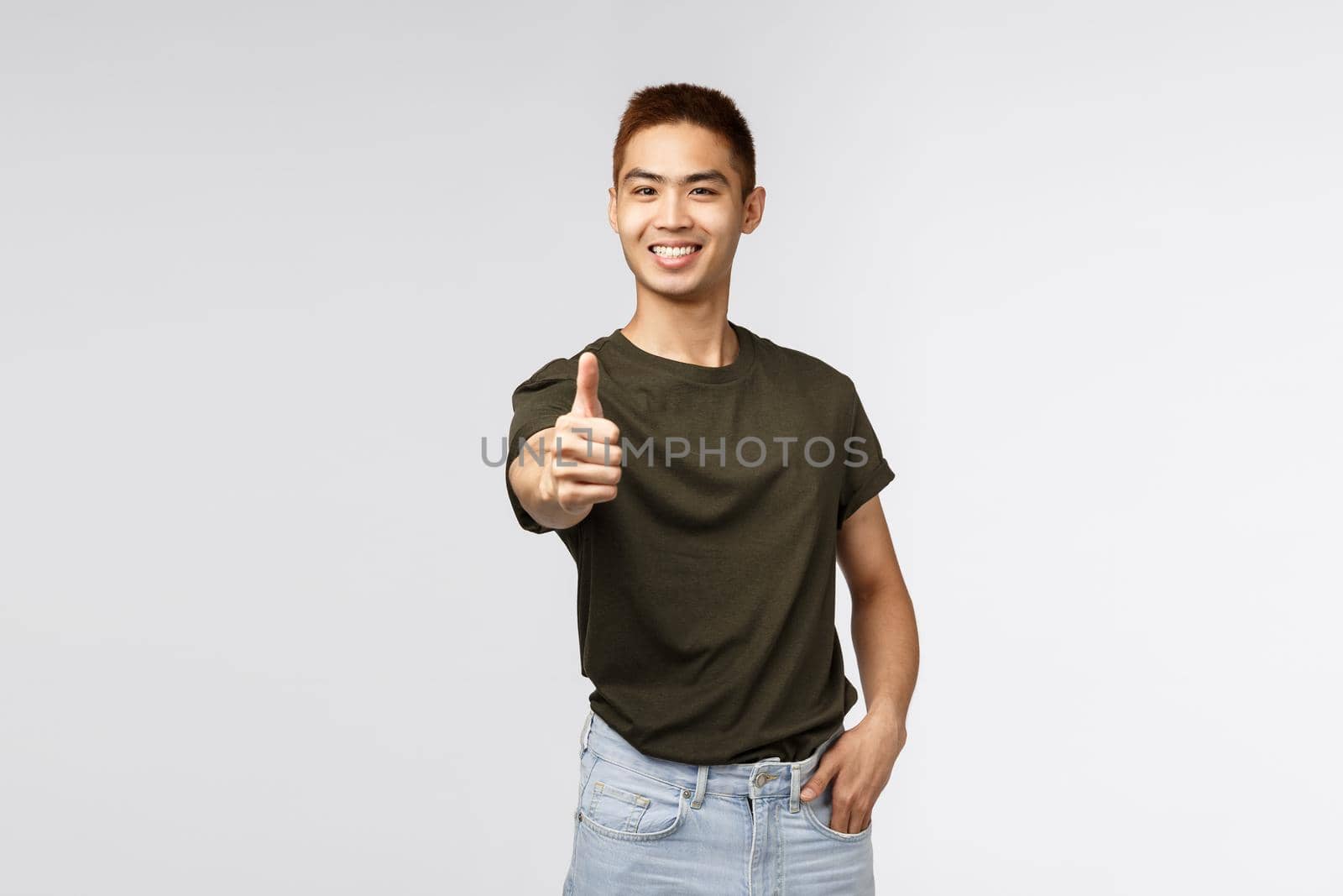 Very good, excellent job. Portrait of happy, pleased asian man thumb-up with extended hand and smiling, encourage keep up nice work, being satisfied and recommend product, grey background.