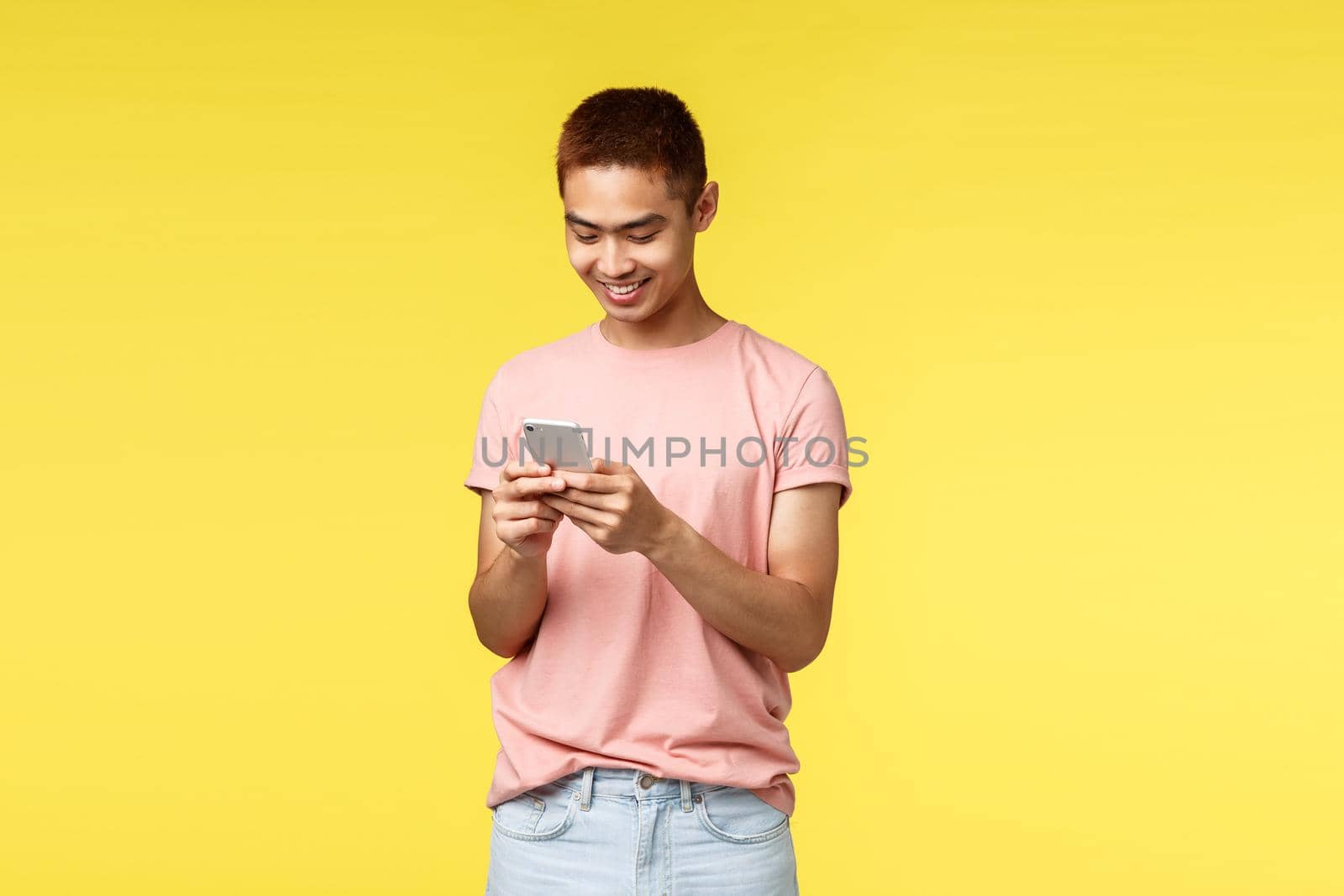 Technology, communication and lifestyle concept. Smiling, enthusiastic handsome asian hipster guy messaging friend, using mobile phone and smiling at smartphone display pleased, texting.