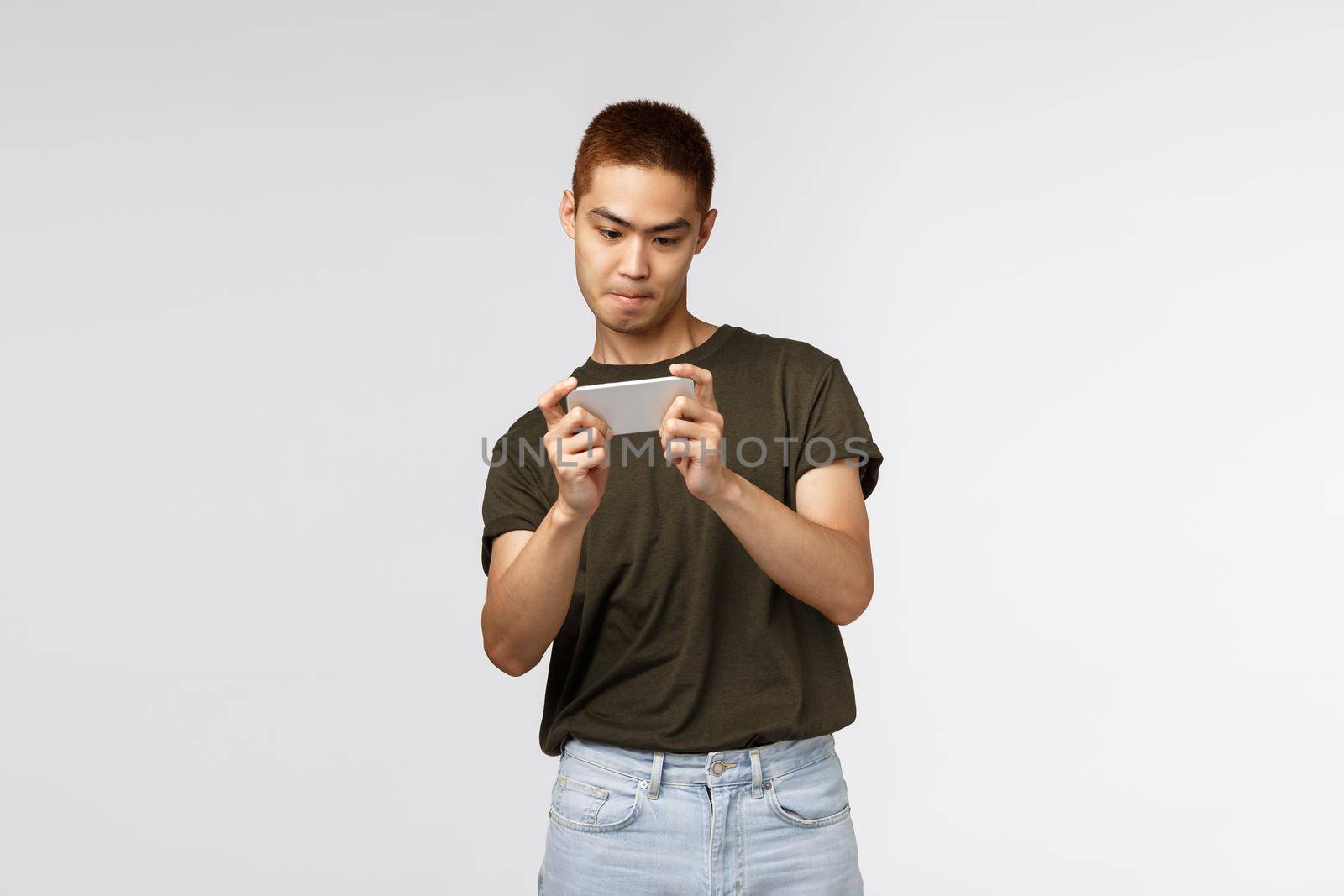 Technology, online lifestyle and communication concept. Portrait of cheerful geeky asian guy staying at home, social-distancing during covid19, download smartphone app, playing racing game.