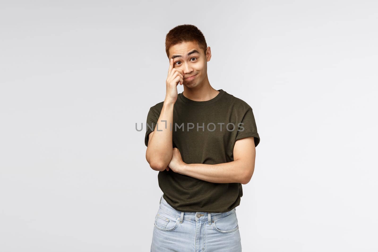 Portrait of bothered and annoyed asian guy hear nonsense, smirk and stare with disbelief, scratching forehead and look camera ignorant, standing grey background distressed and tensed.