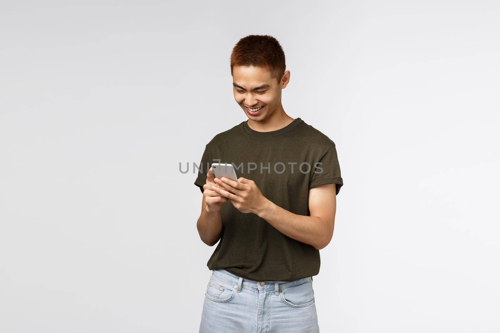 Technology, online lifestyle and communication concept. Cheerful handsome asian male student sending message, subscribe to internet language courses, using mobile phone, scroll news feed by Benzoix