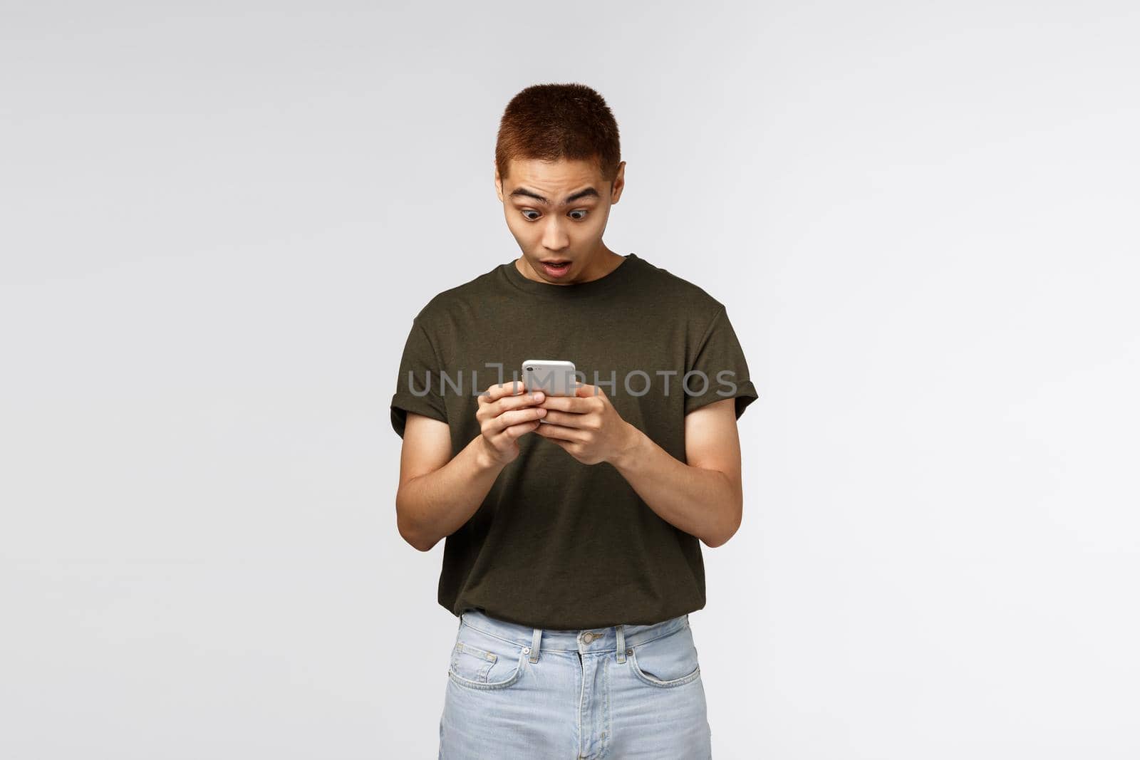 Technology, online lifestyle and communication concept. Surprised taiwanese guy, male student react to amazing news read internet social network, stare at smartphone impressed, use mobile phone.