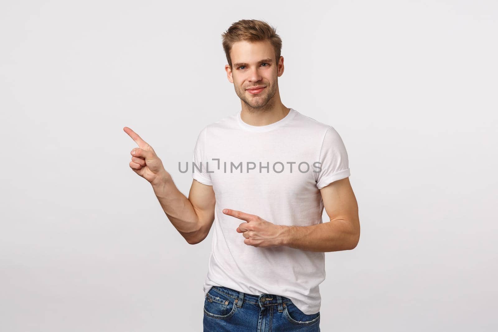 Handsome, assertive pleased young blond man with bristle, pointing upper left corner, smiling as looking partner, discuss business concepts, suggest product, recommend place, white background.