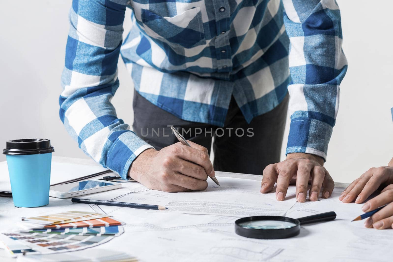 Man writing with pen on technical drawing. Creative team of designers together working with construction blueprint. Thorough study and approval of design project. Architecture studio concept.