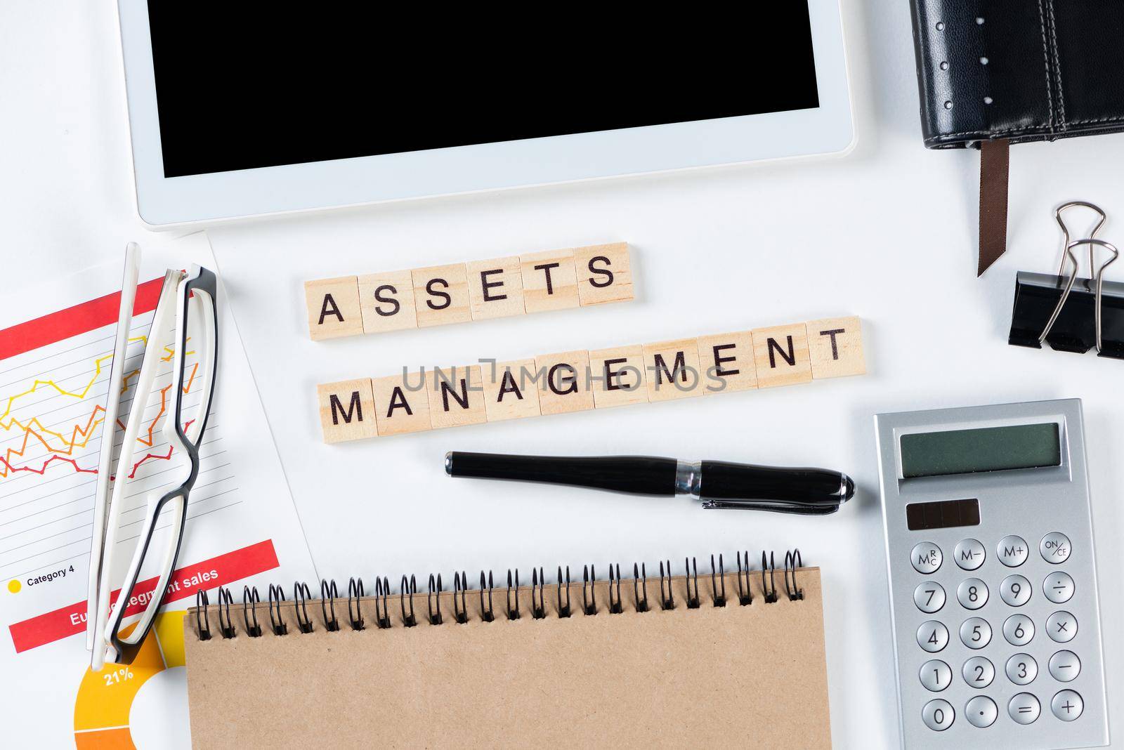 Asset management concept with letters on cubes. Still life of office workplace with supplies. Flat lay white surface with tablet computer, calculator and notepad. Investment strategy and planning.