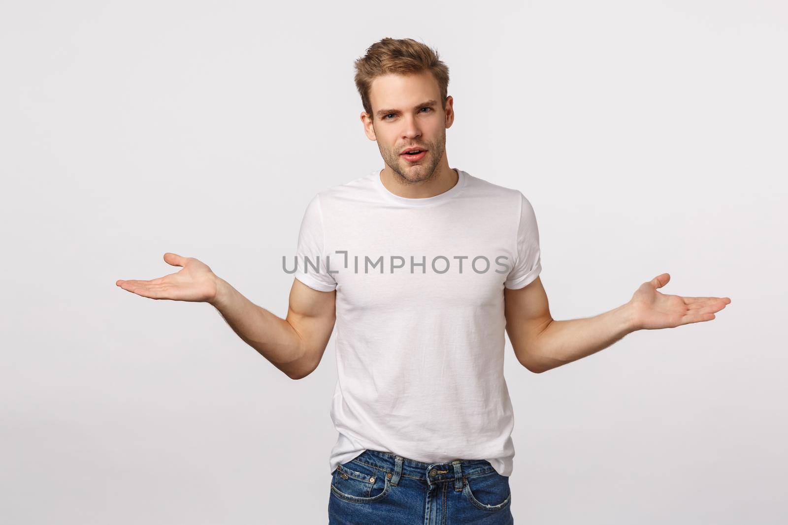 What do you want from me. Annoyed and aggressive questioned, puzzled blond handsome man trying deal with strange accusation, spread hands sideways, stare camera confused, white background.