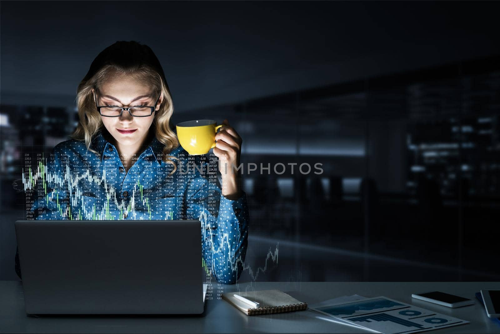 Attractive woman looking at her laptop screen sitting in night office. Mixed media