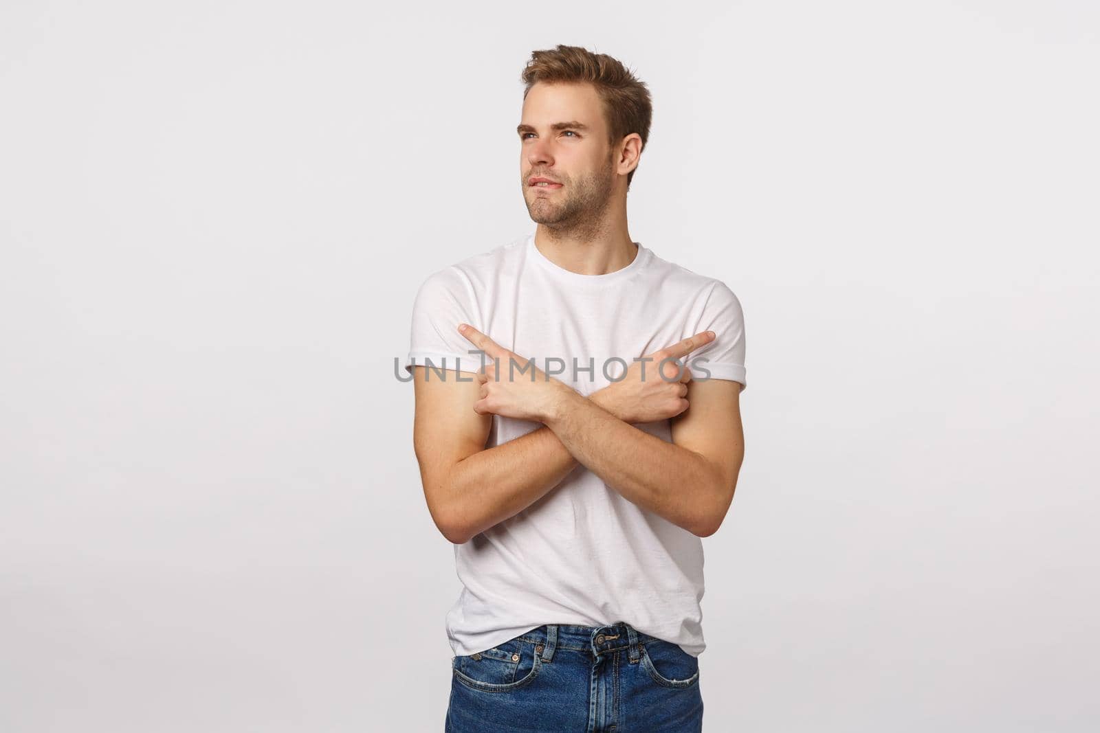 Unsure, thoughtful good-looking blond guy picking between two choices, cross hands pointing sideways left and right, bite lip and squinting as thinking, making decision, white background.