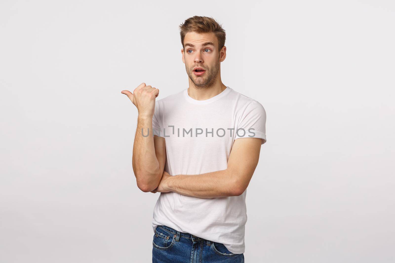 Astounded and impressed cute bearded blond caucasian male in t-shirt, pointing and looking left speechless, getting interested, attend good lecture, standing amazed white background.