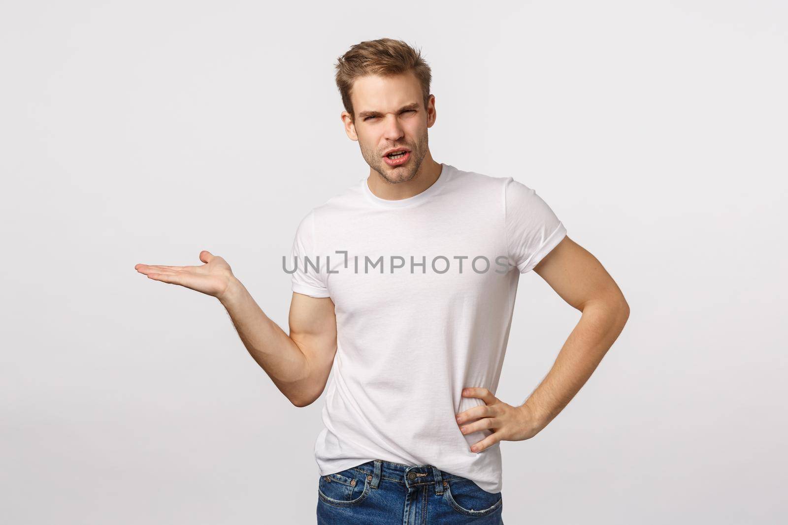 So what, what is this. Sassy and angry, disappointed male boss pointing left with palm and arguing, squinting displeased, judging bad product, look frustrated or upset, white background.