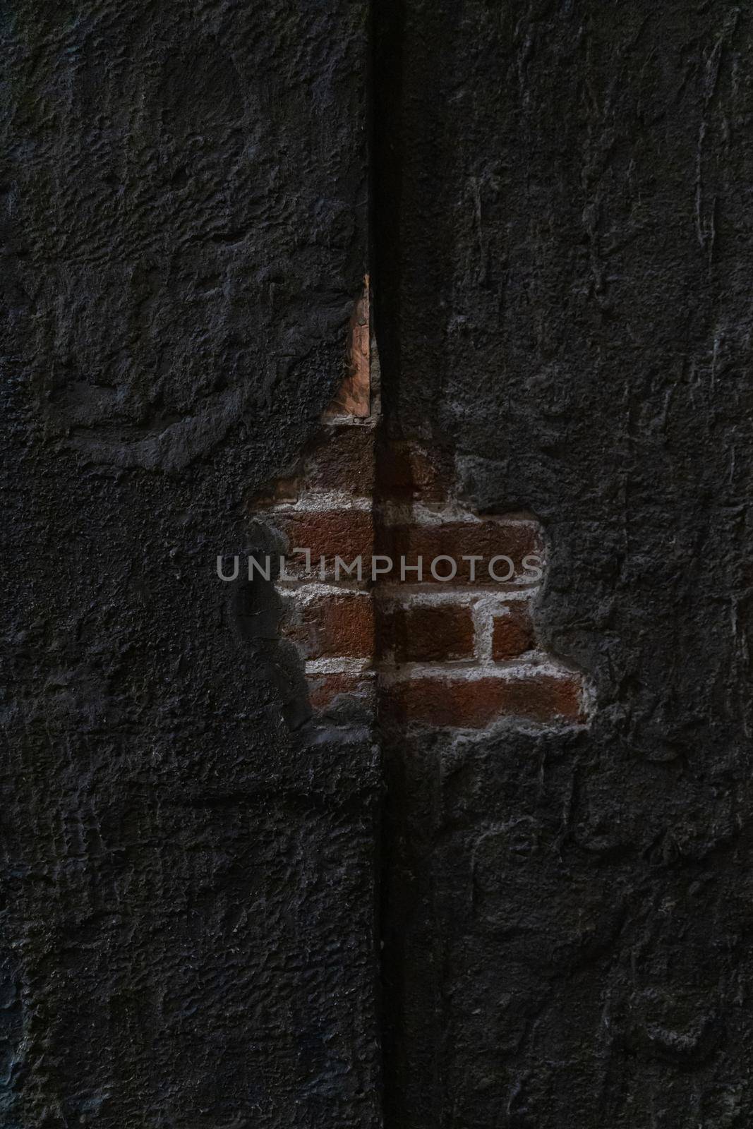 Small hole in concrete wall with exposed old red brick wall