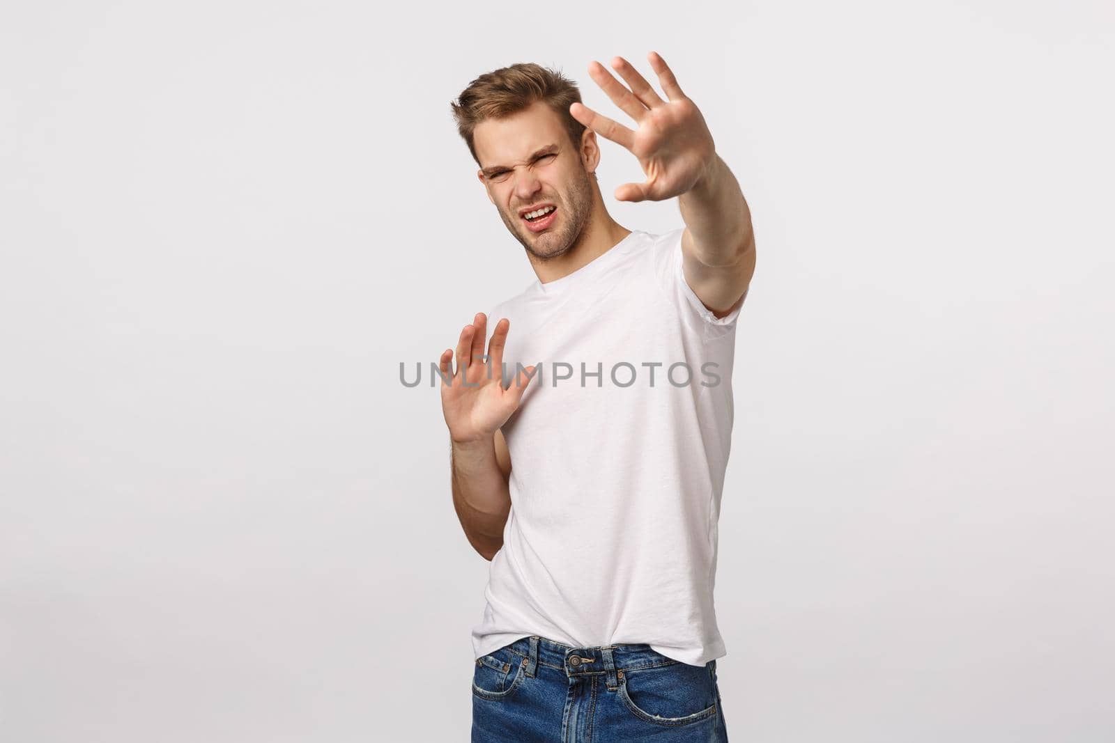 Turn-off that light. Displeased and bothered young handsome man defending himself trying cover something bright with raised hands, squinting discomfort, grimacing, famous person avoiding paparazzi.