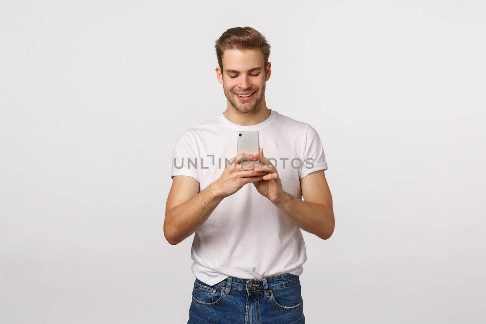 Enthusiastic handsome and cute blond boyfriend taking photo for girlfriend, shooting event, record video on smartphone, holding mobile phone and looking at screen with pleased smile, white background.