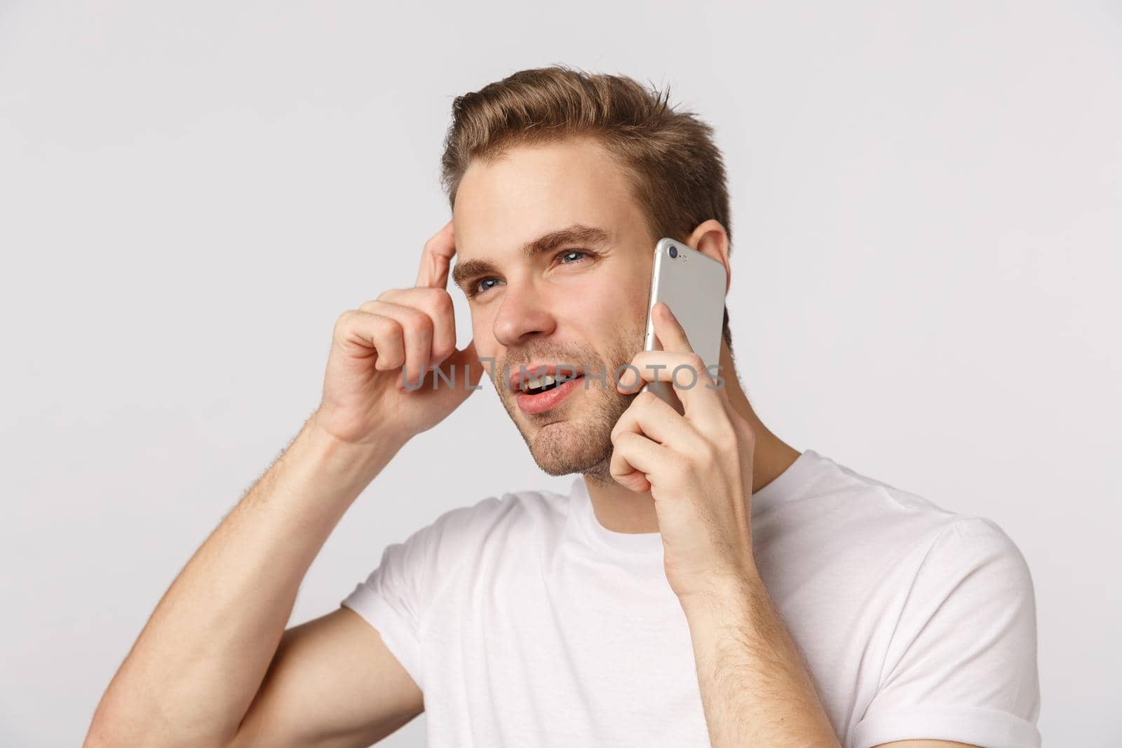 Thoughtful unsure young blond guy speaking on phone, scratching head pensive, thinking what order via mobile, hold smartphone near ear, squinting as pondering what answer, white background.