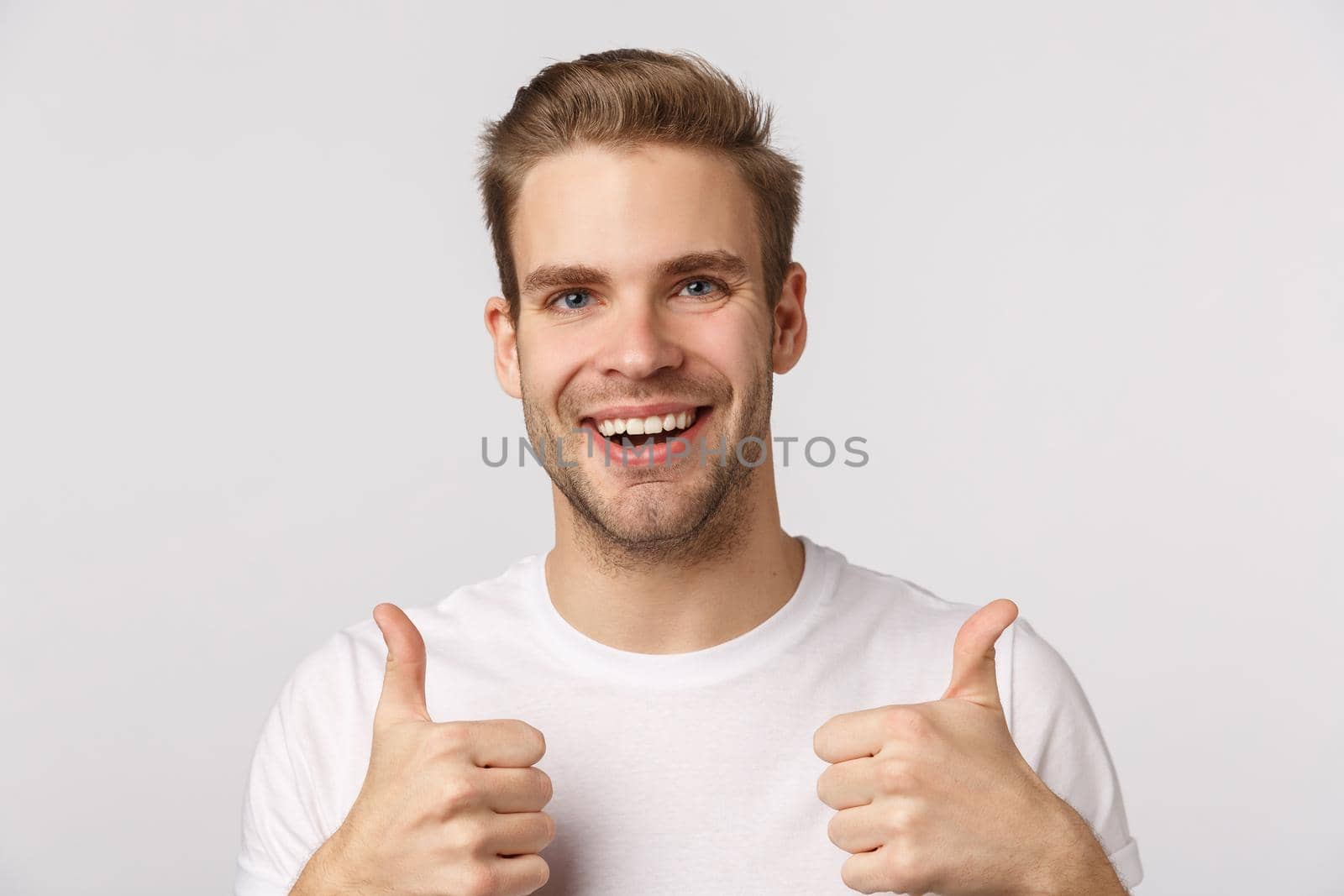 Close-up studio shot positive, pleased blond caucasian guy show thumbs-up and smiling, encourage friend making great choice, recommend product, like idea, approve plan, agree, stand white background.