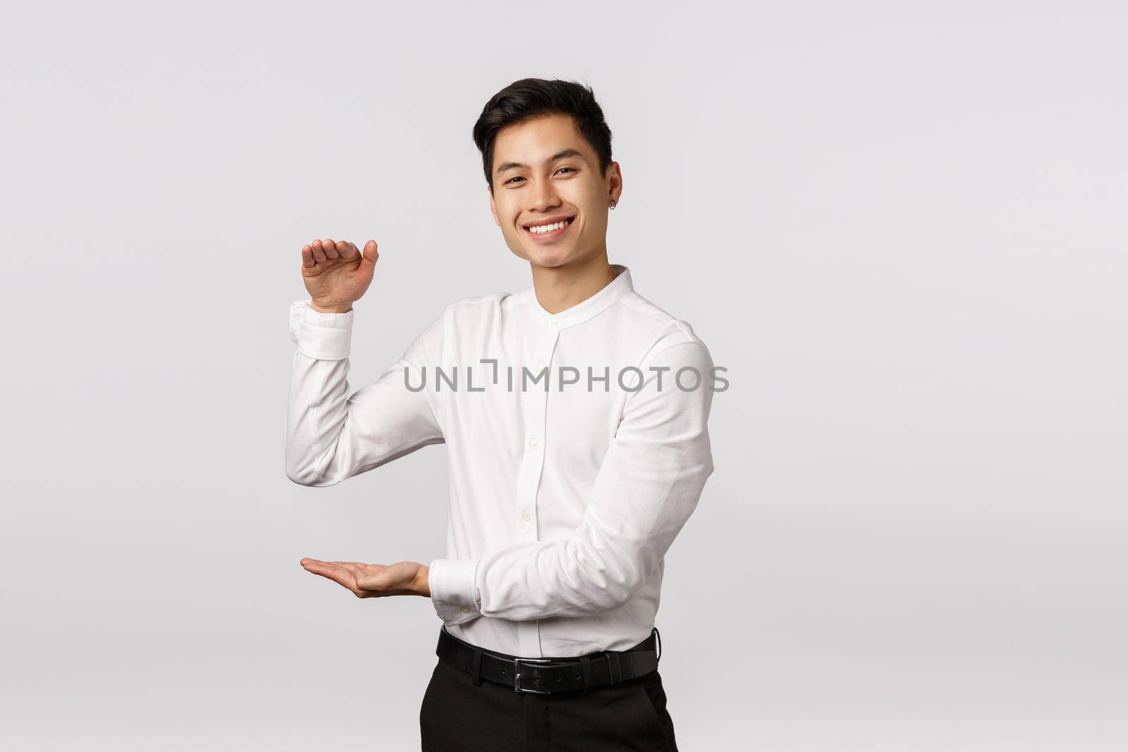 Joyful good-looking asian male entrepeneur, employee in white shirt, pants, showing big box with pleased expression, holding product or something large and satisfying, stand white background.