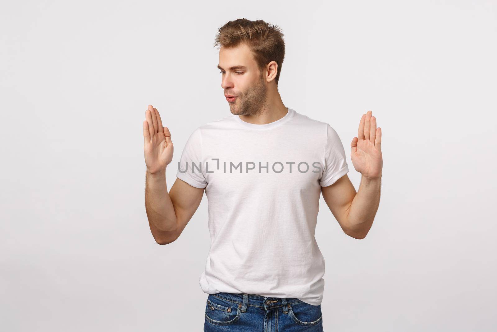 Handsome blond young man amazed with size of product as if holding something large or big, shaping object and observe it, wistle from amazement being impressed, white background.