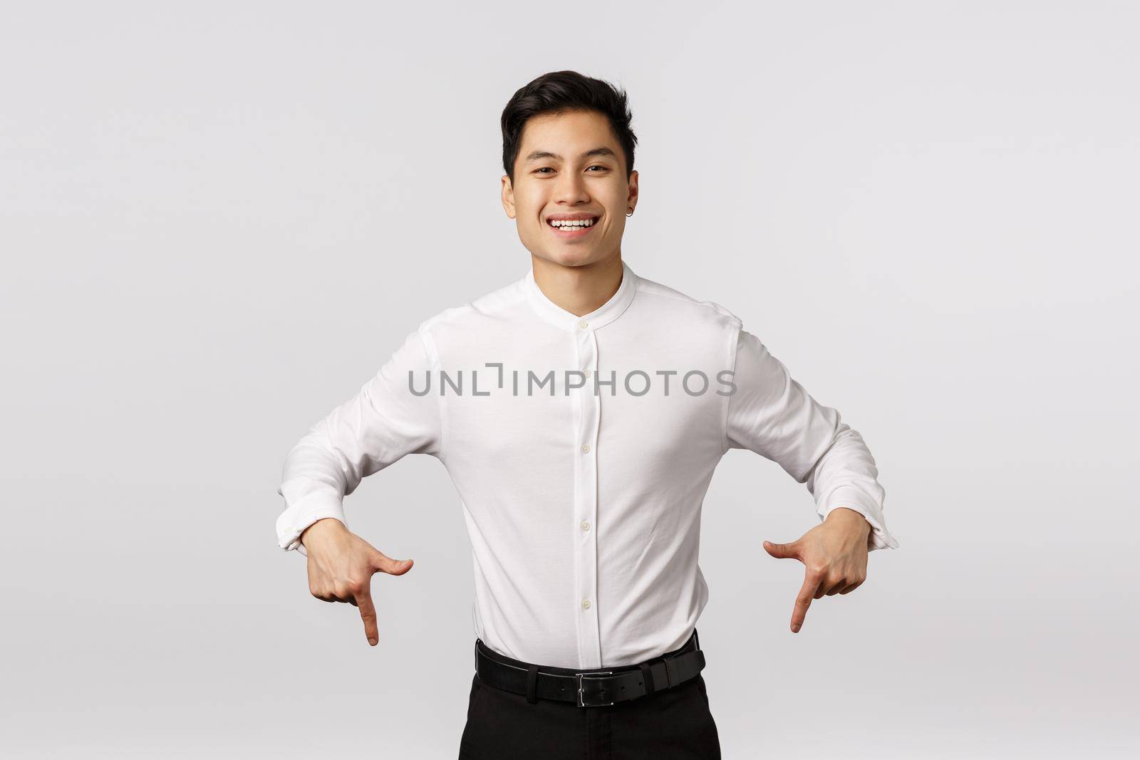 Carefree, smiling cute and joyful asian millennial guy in formal wear, shirt and pants, pointing down, inviting check out, visit event page, shopping site or corporate banner, grinning rejoicing.