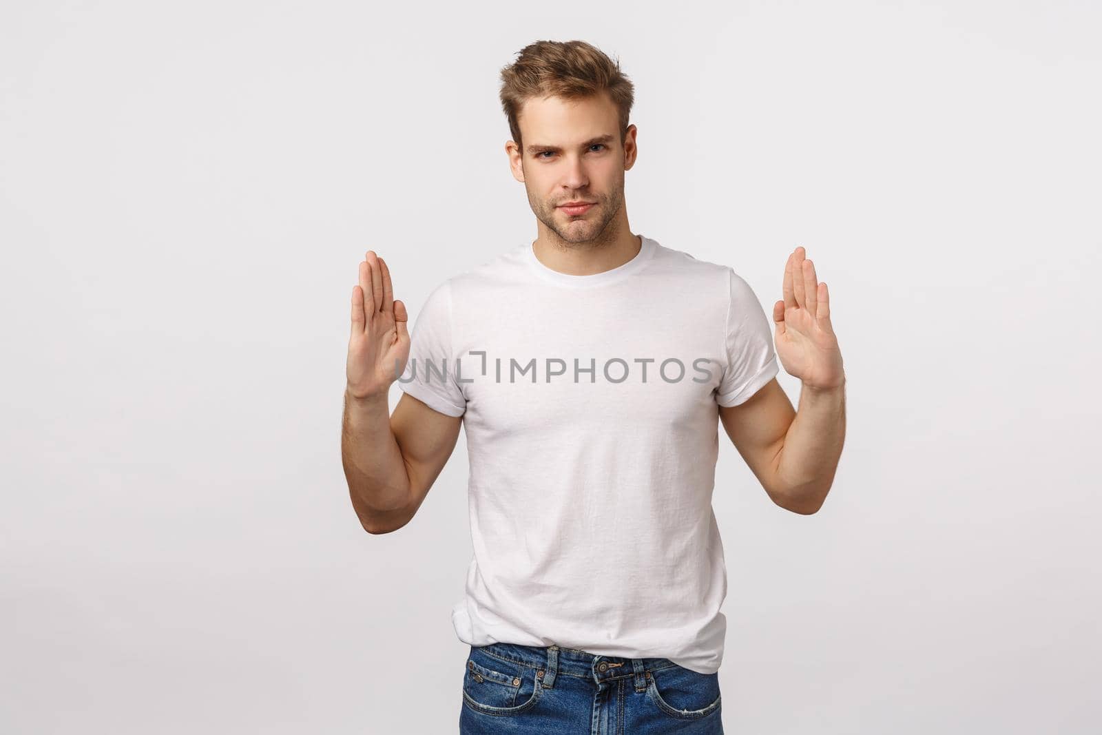 Handsome stylish blond bearded macho man in white t-shirt, raising hands near chest as if holding something, introduce corporate logo, banner or promotion, look assertive and coquettish.