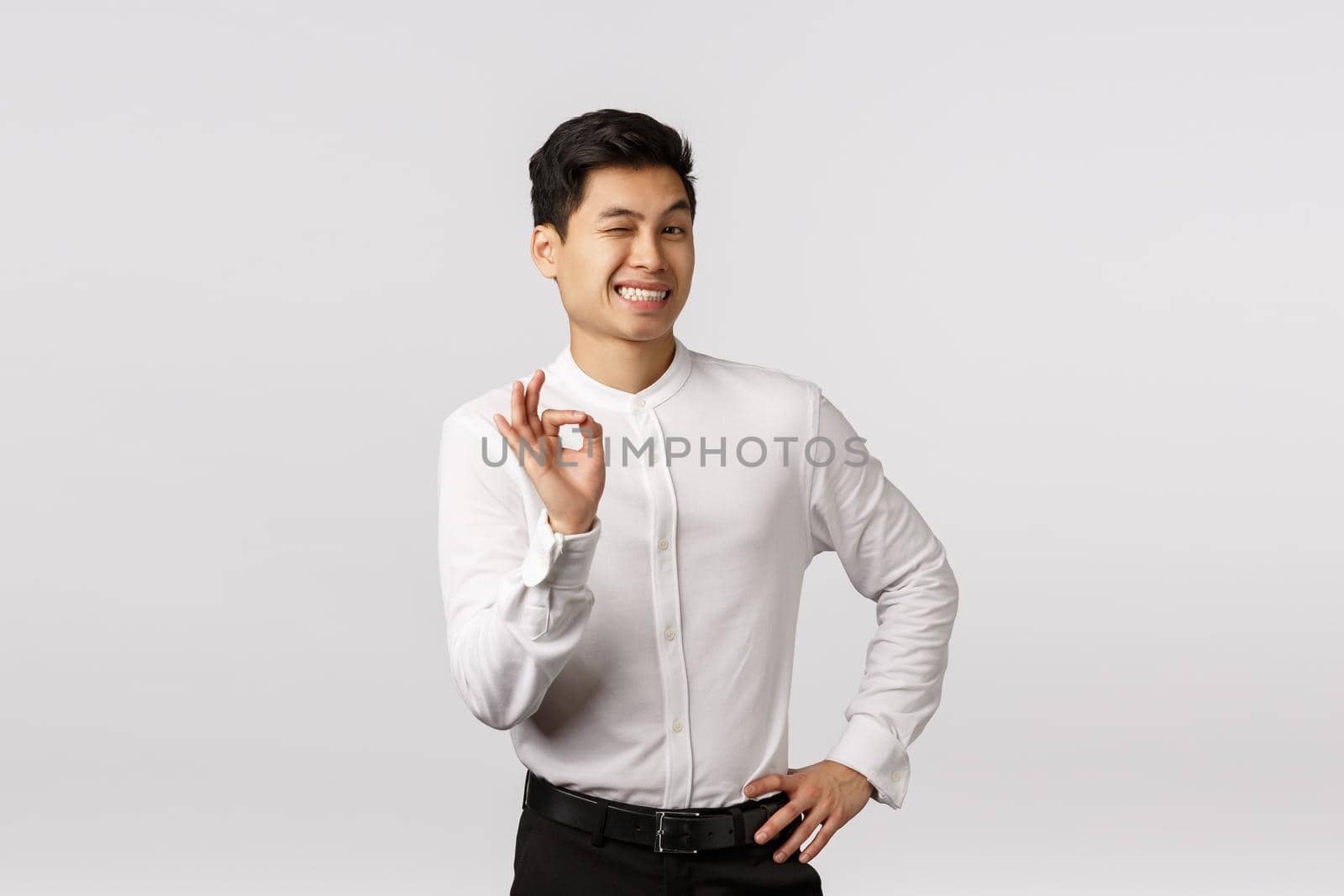 Enthusiastic and creative cute asian male entrepreneur have everything under control, wink cheeky and coquettish, smiling self-assured, showing okay, good, approval gesture, like someones idea.