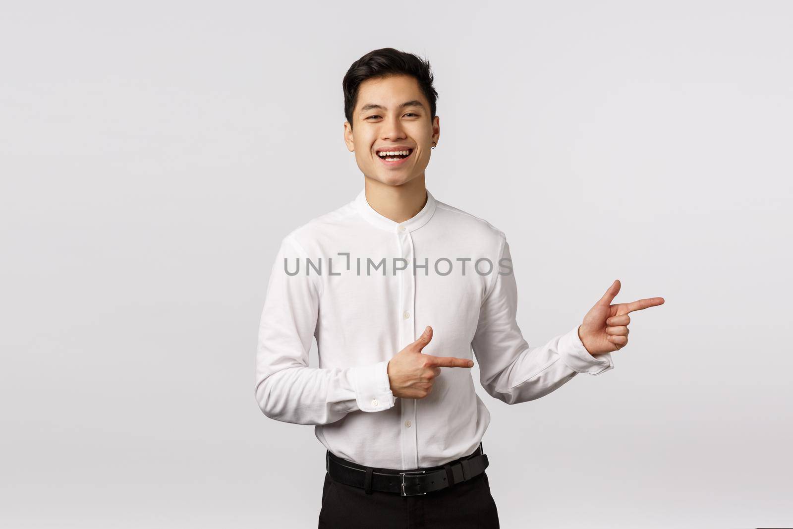 Carefree charismatic asian young 25s man in formal outfit, white shirt, black pants, invite check out and see event banner, pointing right and smiling, laughing amused, standing white background.