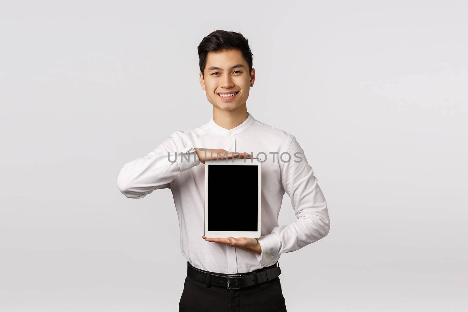 Satisfied handsome asian businessman, showing digital tablet screen over chest and smiling pleased, give promo, advertise gadget application or shopping site, showing corporate link.