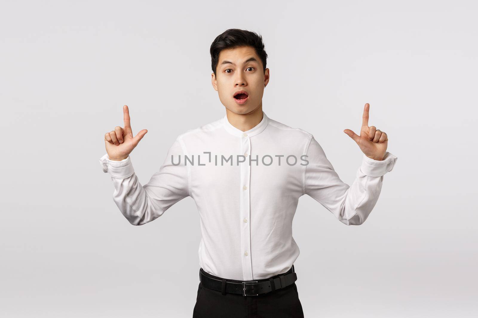 Fascinated, impressed and surprised attractive asian guy with short stylish haircut, wear formal outfit, open mouth in awe, say wow look astonished camera, pointing up to discuss curious thing.